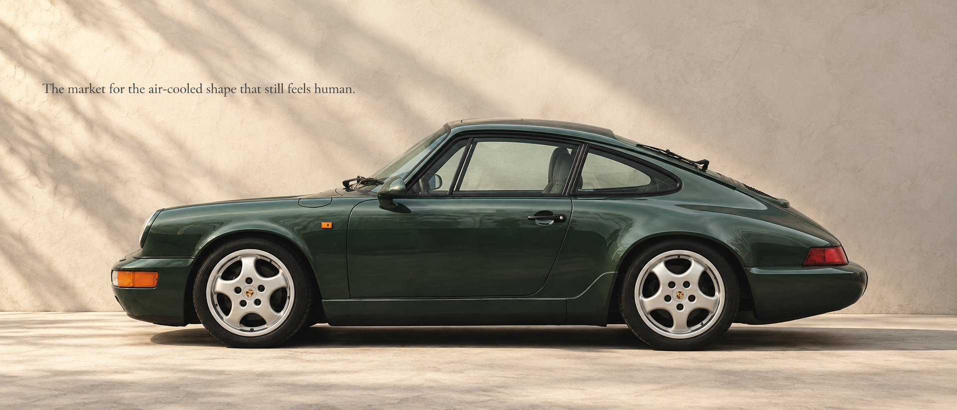 Green Porsche 964 Carrera 2 in side profile beneath soft architectural light
